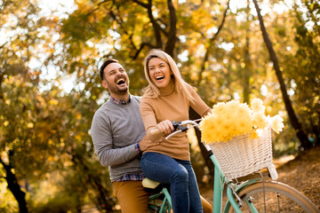 Active young couple enjoying riding bicycle in golden autumn park