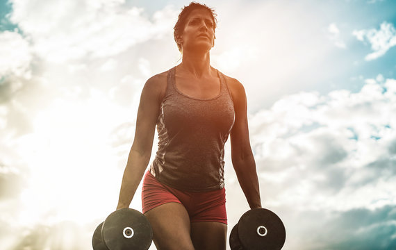Female athlete doing workout session outdoor at sunset - Fitness woman working with dumbbells - Body building and sport trends concept - Focus on her face