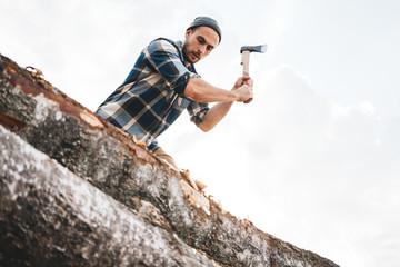 Strong lumberjack in plaid shirt chops tree in wood with sharp ax, close up axe, wood chips fly. Horizontal, blurred Background