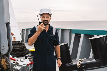 Marine Deck Officer or Chief mate on deck of vessel or ship . He holds VHF walkie-talkie radio in...