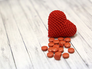 Red pills and knitted heart on light wooden table, selective focus. Concept for hypertension, heart...