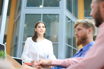 Obraz premium Group of young people in casual wear sitting at the office desk and discussing something while looking at PC together.