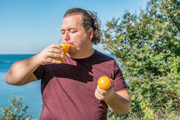 Funny fat man on the ocean drinking juice and eating fruits. Vacation, weight loss and healthy...