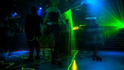 People dancing under green strobe lights in the dark. Entertainment, leisure and nightlife concept. Adult lifestyle.