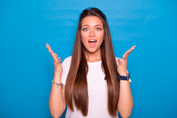 Fototapeta premium Cute brunette woman with long hair posing in white t-shirt on a blue background. Emotional portrait. She smiles in amazement