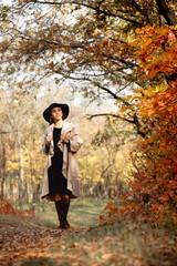 woman in dress and hat on background of autumn foliage