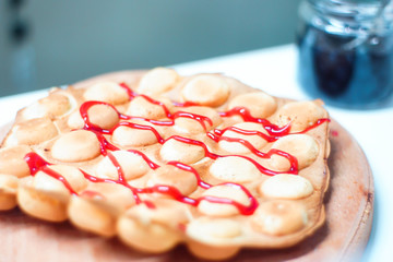Cook prepares Hong Kong waffles with ice cream, jam and fruit. Young woman holding Hong Kong bubble...
