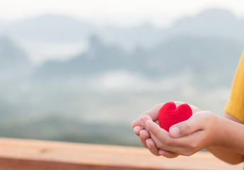 Fototapeta premium Hand boy holds the red heart with mountains landscape. copy space for text. the concept of love, Valentines day, symbol and romantic. red heart for gift.