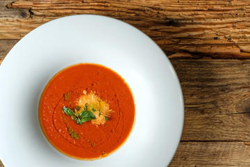 Vegetable tomato soup with cheese and green herbs on rustic wooden background. Top view
