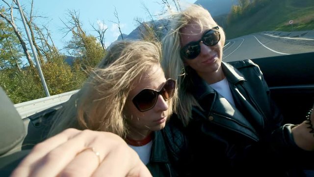 Two young beautiful girls in black glasses and leather jackets ride in a red cabriolet near the high mountains. Life is ruled, get freedom