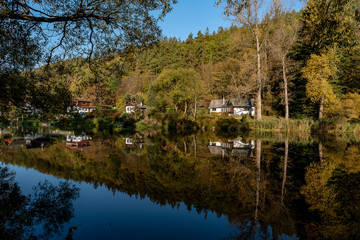 Fototapeta na wymiar houses and trees on the banks of the river, reflecting on the surface in autumn