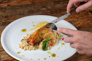 Man's hands holding knife and fork with piece of baked salmon