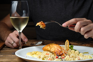 Man's hands holding knife and fork with piece of baked salmon