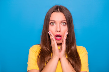 Cute brunette woman with long hair posing in yellow t-shirt on a blue background. Emotional portrait. She shocked, amazed