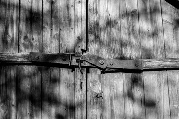Rusty, old, handmade  gate lock  on pine wooden boards close up shot on a bright sunny day,  in black and white.