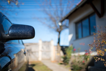 Dirty rear mirror on focus on parking car in front of a residentual house.