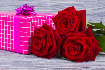Red roses and gift box close up. Pink present box and blooming flowers on rustic wood. Happy Valentines Day. Mothers Day background.