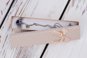 Gift box with necklace on wooden background. Silver owl pendant in jewelry gift box. Luxury gift...