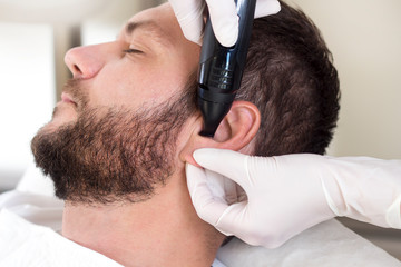 Mężczyzna w salonie kosmetycznym podczas zabiegu usuwania owłosienia z uszu.