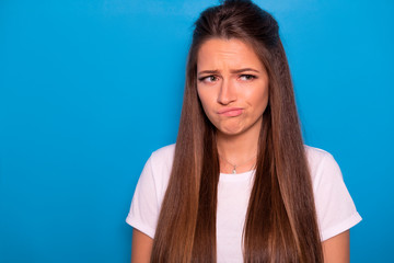 Cute brunette woman with long hair posing in white t-shirt on a blue background. Emotional...