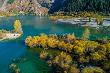 Beautiful turquoise color lake Issyk in mountainous area of Almaty region during colorful autumn with yellow birches and pine trees, Kazakhstan