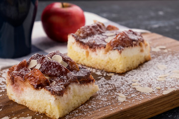Homemade apple pie slice with  almond flakes and icing sugar on wooden board