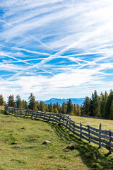 Obraz premium Weidezaun aus Holz auf Almwiese mit vielen Kondensstreifen am Himmel