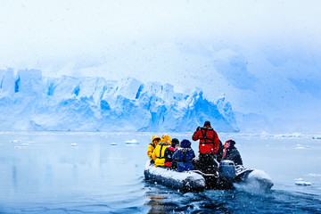 Snowfall over the boat with frozen tourists driving towards the huge blue glacier wall in the background, near Almirante Brown, Antarctic peninsula