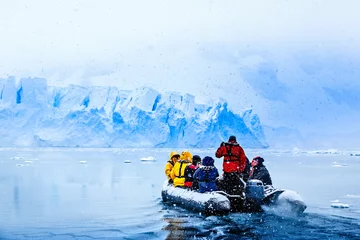 Foto auf Acrylglas Antarktis Schneefall über dem Boot mit gefrorenen Touristen, die in Richtung der riesigen blauen Gletscherwand im Hintergrund fahren, in der Nähe von Almirante Brown, antarktische Halbinsel