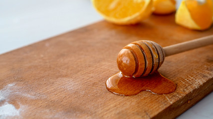 Łyżka z ociekającym miodem leżąca na drewnianej desce w towarzystwie pokrojonych pomarańczy