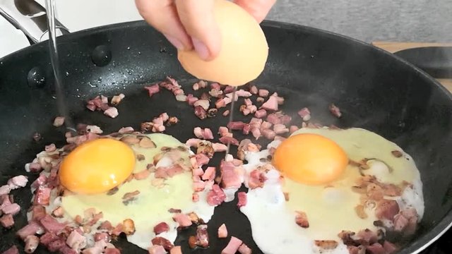 Frau schl&auml;gt Eier zu Speck in die Pfanne, Spiegeleier braten, full HD 1080p Video Footage