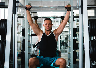 A Handsome man squats in a gym, view on the reflection in the mirror