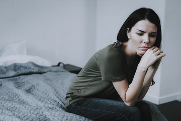 Portrait of Sad Dark-Haired Woman Sits on Bed