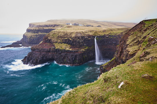 Scenic landscape picture on the vilage Gasadalur on the Vagar island one of the Faroe Islands with green meadows, wild atlantic ocean, high clifs and beautiful waterfall