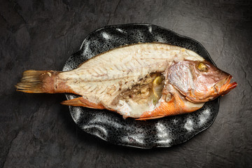 Half eating red snapper fish with exposed bones, on dark background, top view
