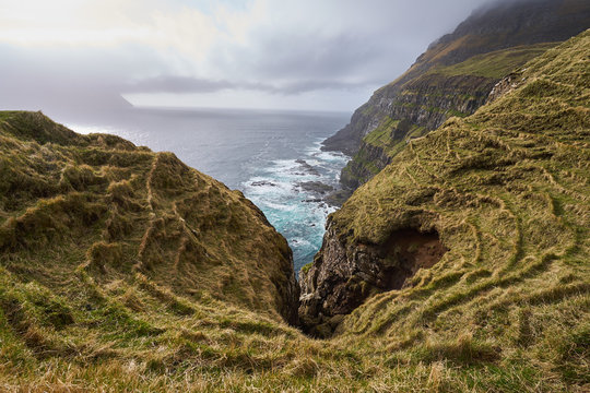 Rocky coast, high cliffs and wild atlantic ocean before rain in Faroe island Vagar. Picture taken from top of the cliff from meadow dedicated for sheep pasture.
