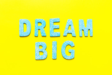 Word DREAM BIG  made out of small blue wooden letter on yellow background, flat lay