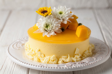 Obraz na płótnie Canvas Mango cheesecake with yellow jelly topping, with flowers and fresh mango pieces on white background, horizontal composition