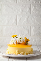 Mango cheesecake with yellow jelly topping, with flowers and fresh mango pieces on white background, vertical composition