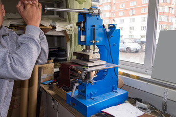 The man in the workshop presses the lever on the press machine to get the embossed logo and letters on the leather product that heats the cliche and squeezes the desired image on the material