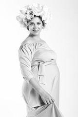 Beautiful pregnant woman in dress and flower wreath. On a white background. Black and white photo in bright tonality.
