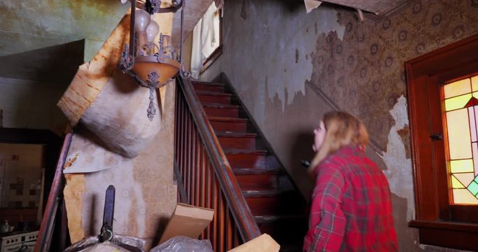 A man and woman walk up the steps of an old abandoned home, looking for antiques and treasures. Wallpaper is falling off the walls.  	