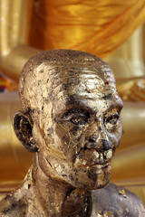 Statue of a monk with head and face covered in gold leaf at a Buddhist temple in south east Asia.