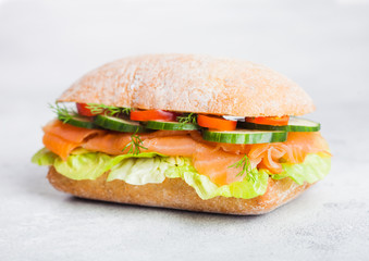Fresh healthy salmon sandwich with lettuce and cucumber on white stone background. Breakfast snack. Diet food