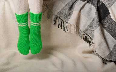 Female legs in warm white knitted tights and green socks on a white background made of faux fur