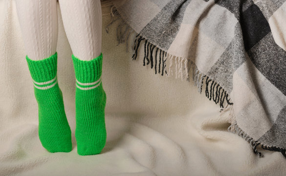 Female legs in warm white knitted tights and green socks on a white background made of faux fur
