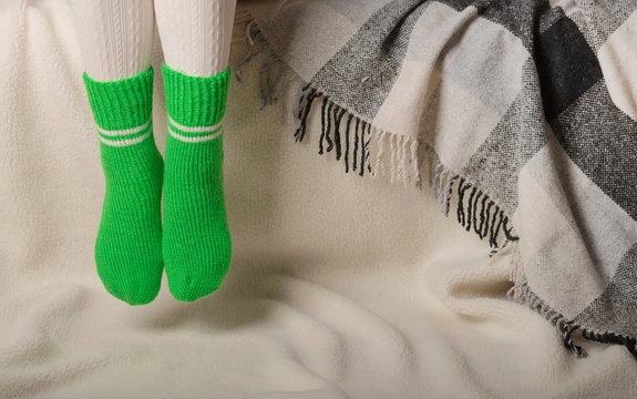 Female legs in warm white knitted tights and green socks on a white background made of faux fur
