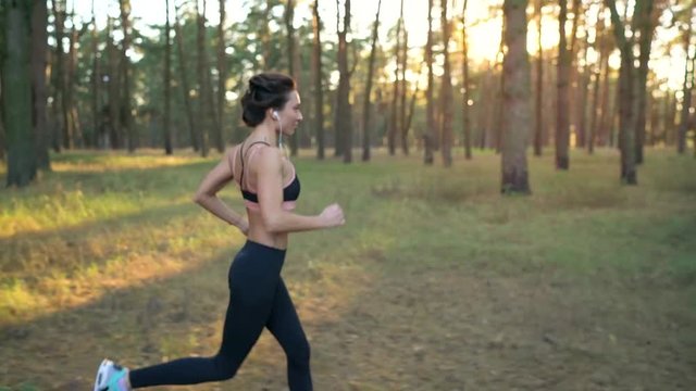Close up of woman with headphones running through an autumn forest at sunset. Filmed at different speeds - normal and slow motion