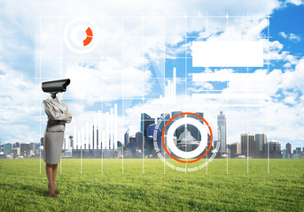 Camera headed woman standing on green grass against modern cityscape