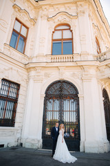 Couple walk near the big palace. Elegant groom and bride in their wedding clothes. Love